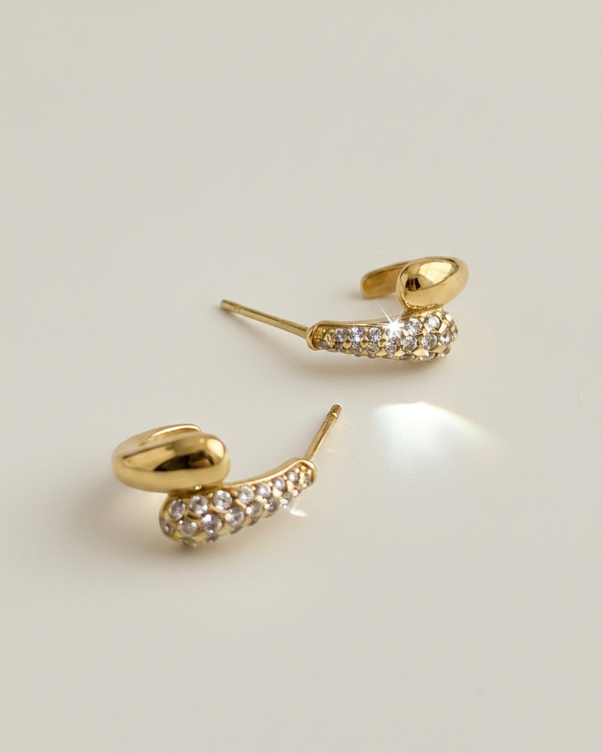 Pendiente de acero inoxidable y oro de 18k con diseño orgánico y pavé de circonitas blancas brillantes sobre fondo neutro, estilo minimalista de lujo.